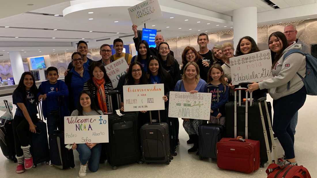 A group of students from Honduras and St. Augustine's congregants meeting in an airport with welcome signs.